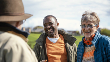 A man and a woman stood together, smiling whilst talking to another man in a field